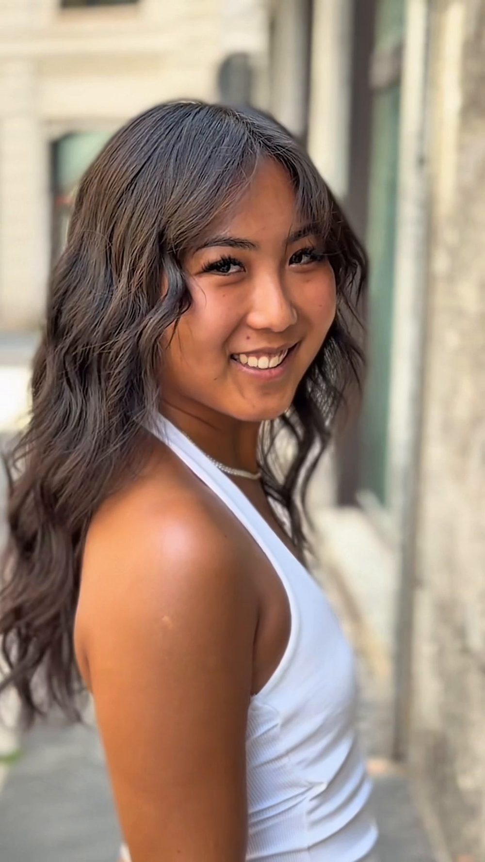 Onde scure lunghe e voluminose, ragazza sorridente in strada